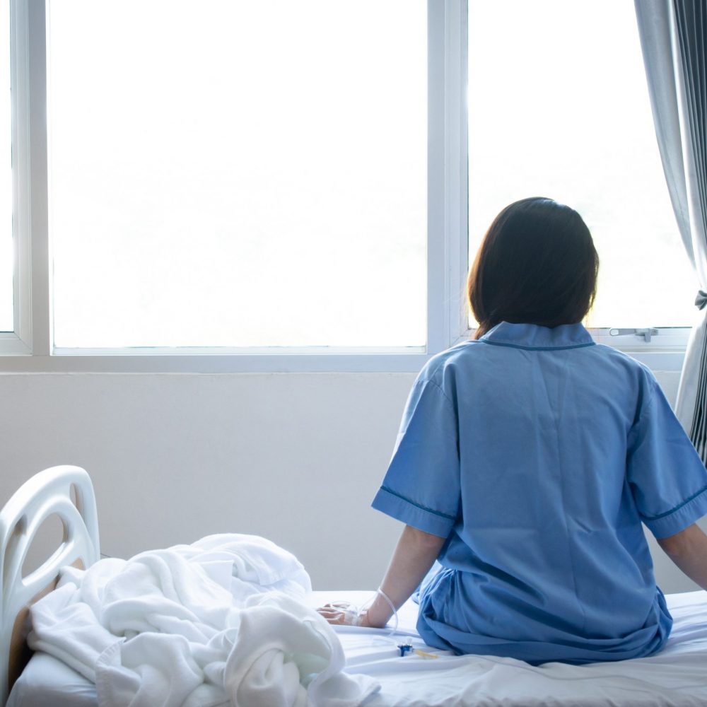 Back,View,Of,Patient,Woman,Sitting,On,Bed,In,Hospital